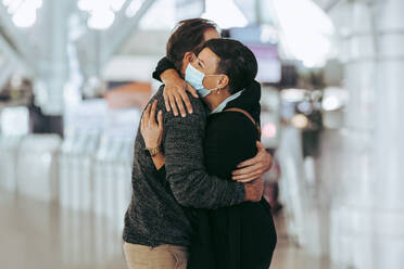 Frau empfängt Mann am Flughafen während der Pandemie. Reisendes Paar nach langer Trennung trifft sich am Ankunftsgate des Flughafens. - JLPSF06049