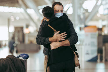 Ein Mann umarmt eine Frau nach der Ankunft von einer Reise nach einer Pandemie am Flughafen. Ein Paar trifft sich bei der Ankunft nach langer Trennung während der Pandemie am Flughafen. - JLPSF06051