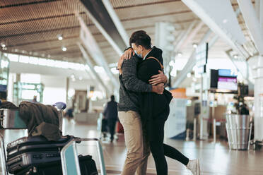 Verliebtes Paar, das sich am Flughafen umarmt, nachdem der Mann von einer Reise zurückgekehrt ist. Frau umarmt Mann nach Ankunft von einer Reise während einer Pandemie. - JLPSF06053