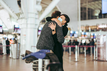 Woman meeting husband after long separation during covid-19 pandemic at airport arrival gate. Female wearing face mask welcoming her man at airport arrival. - JLPSF06057