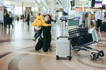 Frau mit Gesichtsmaske umarmt ihren Sohn am Flughafen während der Pandemie. Mutter, die von einer Reise zurückkommt, wird von ihrem Sohn am Flughafen empfangen. - JLPSF06065