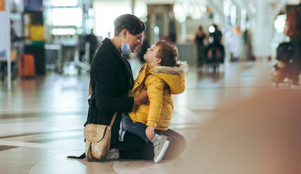 Liebevolle Mutter und Sohn am Flughafen: Mutter mit Gesichtsmaske hält ihren Sohn nach der Ankunft aus dem Ausland während der Pandemie. - JLPSF06070