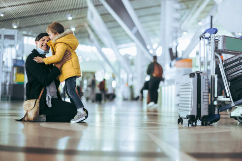 Mutter und Kind treffen sich am Flughafen nach einer Pandemie. Frau mit Gesichtsmaske trifft ihren Sohn nach der Ankunft von einer Reise am Flughafen. - JLPSF06072