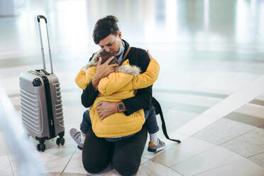 Mutter, die ihr Kind am Flughafen umarmt und küsst. Reisende Frau auf dem Boden, die ihren Sohn am Flughafen nach einer Pandemie trifft. - JLPSF06075