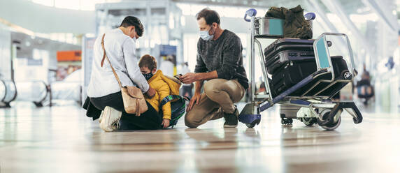 Weitwinkelaufnahme einer Frau, die ihren Sohn und ihren Ehemann am Flughafen nach einer Pandemie trifft. Familie bei der Ankunft am Flughafen mit Gepäck an der Seite. - JLPSF06076