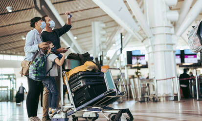 Eine Familie, die während der Pandemie auf dem Flughafen wartet und sich die Abflugtafel ansieht. Eine Familie auf Reisen während der Pandemie. - JLPSF06079