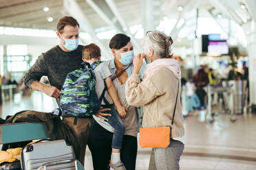 Senior woman meeting her family arriving at airport post pandemic lockdown. Family of three wearing face mask meeting grandmother at airport. - JLPSF06100