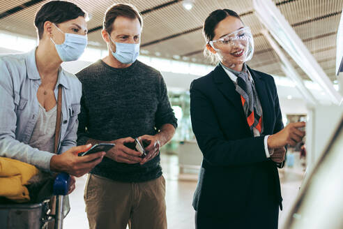 Flughafenpersonal hilft einer Familie beim Self-Service-Check-in während der Pandemie. Passagierfamilie wird von Flugbegleitern am Flughafen während der Pandemie geholfen. - JLPSF06110