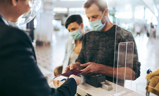 Reisender, der seinen Pass am Check-in-Schalter eines Flughafens während einer Pandemie abgibt. Ein Mann steht am Check-in-Schalter eines Flughafens. - JLPSF06116