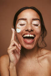 Porträt einer jungen Frau mit Vitiligo, die sich die Wange eincremt. Eine fröhliche Frau mit Vitiligo, die für Selbstakzeptanz und Körperbewusstsein steht. - JLPSF06144