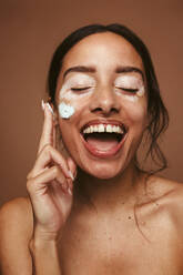 Portrait of young woman with vitiligo applying cream on cheek. Cheerful woman with vitiligo representing self acceptance and body positivity. - JLPSF06144