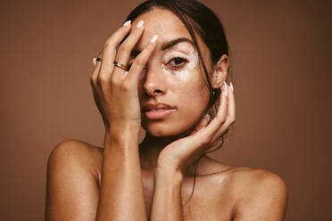 Porträt einer jungen Frau mit Vitiligo auf braunem Hintergrund. Nahaufnahme einer Frau mit Hautkrankheit, die ihr Gesicht mit der Hand bedeckt. - JLPSF06174