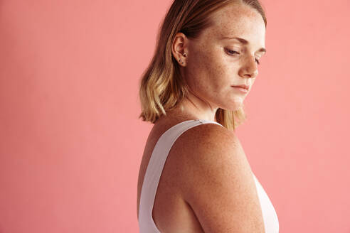 Portrait of young woman with freckles on body standing against brown background. Close up of young woman with freckles all over her body - JLPSF06205