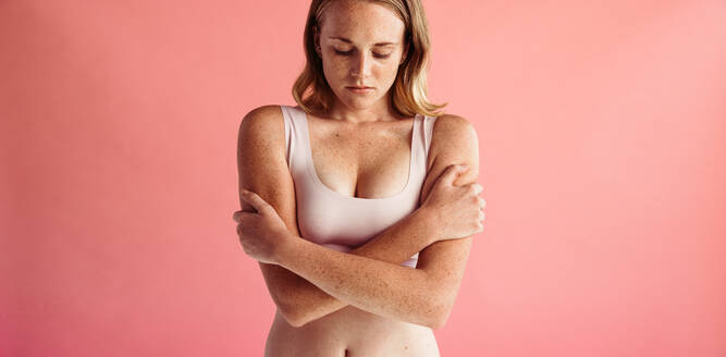 Portrait of young woman with freckled skin standing on peach background with crossed arms. Woman with freckes on body - JLPSF06207