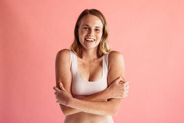 Portrait of young confident woman with freckles. Woman standing with arms crossed on peach background. - JLPSF06209