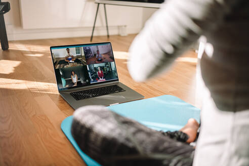 Blick auf eine Frau, die einen virtuellen Fitnesskurs mit einer Gruppe von Menschen zu Hause per Videokonferenz abhält. Fitnesslehrer, der Online-Yoga-Kurse über einen Videoanruf im Laptop abhält. - JLPSF06313