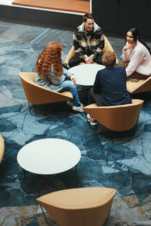 Gruppe von Studenten, die sich unterhalten und um einen Tisch in einem College-Campus sitzen. Junge Leute in der Lobby eines College-Campus. - JLPSF06329