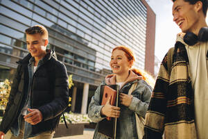 Mädchen, das mit Freunden in der Uni im Freien spazieren geht. Freunde in der Uni gehen nach dem Unterricht nach Hause. - JLPSF06332