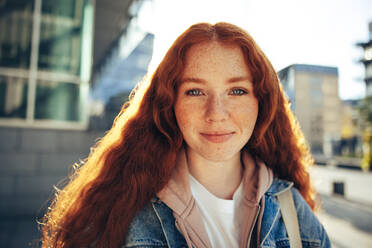 Porträt einer jungen Frau in Freizeitkleidung und mit rot gefärbtem Haar im Freien, eine Studentin steht draußen und schaut in die Kamera. - JLPSF06341