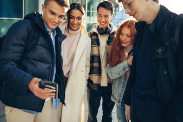 Gruppe von Freunden, die auf ein Handy schauen, Studenten, die im Freien telefonieren. - JLPSF06342