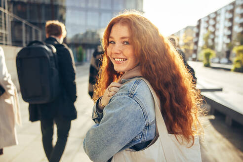 Beautiful young woman going for college. Cheerful student walking toward her class and looking behind. - JLPSF06345