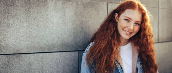 Young female student looking at camera outdoors. Dyed hair girl standing by a wall. - JLPSF06348