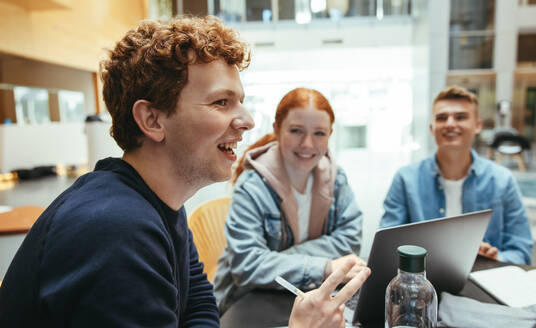 Junge Studentin, die ihren Freunden bei Gruppenstudien auf dem College-Campus hilft. Junge lächelt beim Lernen mit Klassenkameraden in der High School. - JLPSF06358