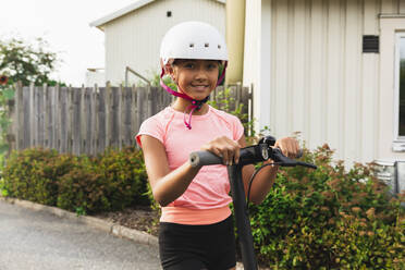Lächelndes Mädchen mit Helm, das mit einem Tretroller steht - DMMF00136