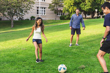 Happy family playing football on grass in lawn - DMMF00162