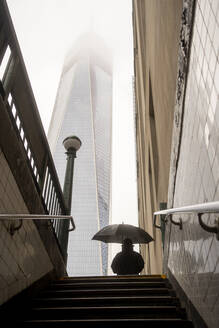 USA, New York, New York City, Fußgänger mit Regenschirm vor U-Bahn-Eingang mit nebelverhangenem Wolkenkratzer im Hintergrund - MMPF00315