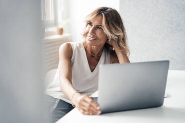 Contemplative businesswoman with laptop at office - JOSEF14083