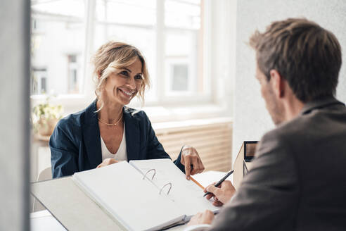 Smiling real estate agent assisting customer signing agreement at office - JOSEF14128