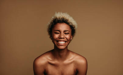 Close up of african american woman laughing. Woman with short curly hair on brown background. - JLPSF06391