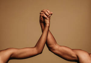 Beschnittene Aufnahme von zwei Armen, die sich gegenseitig halten, als Symbol der Einheit. Männliche und weibliche Hände halten sich gegenseitig. - JLPSF06394