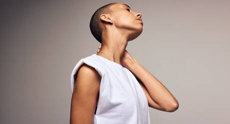 Androgynous female with shaved head standing against colored background. Woman with hand on neck and eyes closed. - JLPSF06441