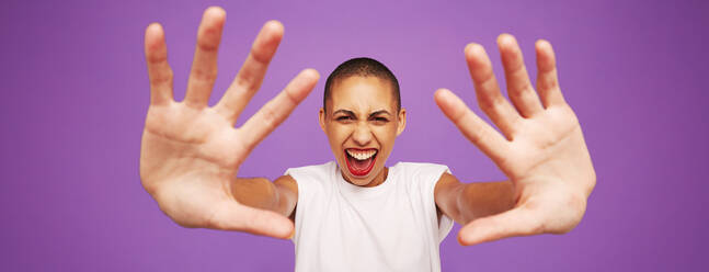 Wide angle portrait of a happy looking woman on purple background. Female model with shaved head and hands in front. - JLPSF06534