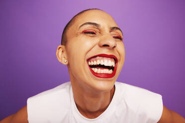 Close up of cheerful woman with colorful makeup. Comical portrait of a female model with makeup laughing on grey background. - JLPSF06538