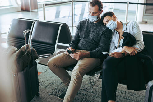 Ein Paar mit Gesichtsmasken sitzt im Wartebereich eines Flughafens. Ein müdes Touristenpaar mit Gesichtsmasken wartet im Flughafen auf einen verspäteten Flug wegen der Abriegelung des Covid-19. - JLPSF06567