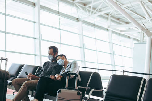 Mann und Frau mit Gesichtsmasken im Wartebereich des Flughafens. Ehepaar am Flughafen während der Abriegelung durch das Corona-Virus. - JLPSF06569