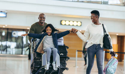 Eine dreiköpfige Familie auf dem Weg in den Urlaub am Flughafen. Eine afrikanische Familie, die sich am Flughafen-Terminal amüsiert. - JLPSF06577