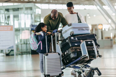 Afrikanische Eltern unterhalten sich mit ihrer kleinen Tochter am Flughafen, während sie auf ihren Flug warten. Dreiköpfige Familie am Flughafen, die sich beim Warten am Flughafen amüsiert. - JLPSF06579