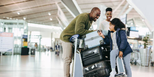 Vater und Mutter warten mit ihrer kleinen Tochter am Flughafen. Touristenfamilie am Flughafenterminal mit Urlaubsgepäck. - JLPSF06587