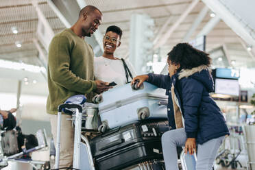 Vater und Mutter unterhalten sich mit ihrer Tochter beim Warten am Flughafen. Afrikanische Familie auf dem Weg in den Urlaub, die auf ihren Flug wartet. - JLPSF06588