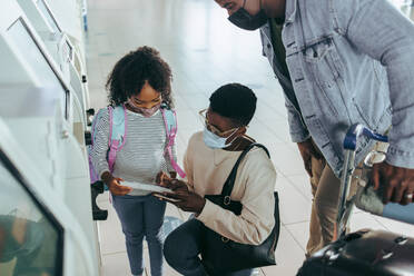 Dreiköpfige Touristenfamilie mit Bordkarte im Flughafenterminal. Mädchen und Mutter betrachten Flugticket mit Vater am Flughafen. - JLPSF06593