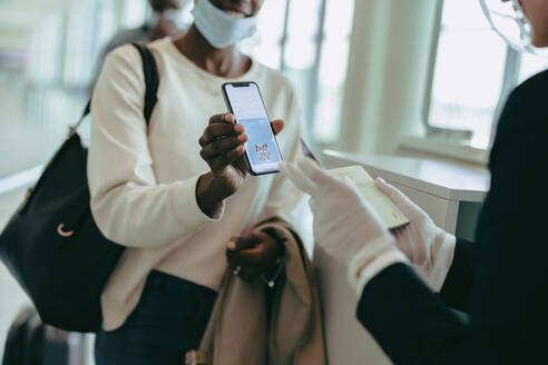 Weiblicher Passagier zeigt dem Flughafenpersonal den Krankenschein. Bodenpersonal kontrolliert den Krankenschein eines Passagiers, der während der Pandemie eincheckt. - JLPSF06597