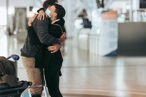 Frau mit Gesichtsmaske umarmt Mann am Ankunftsgate des Flughafens. Frau umarmt und begrüßt Mann nach Pandemie am Flughafen. - JLPSF06602