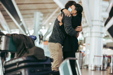 Husband and wife meeting after long separation during covid-19 outbreak at airport arrival gate. Female with face mask welcoming male traveler at airport arrival. - JLPSF06603