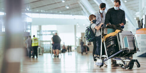 Ehepaar mit Sohn geht am Flughafen spazieren und schiebt Gepäckwagen. Familie am Flughafen auf Reisen während der Pandemie. - JLPSF06609