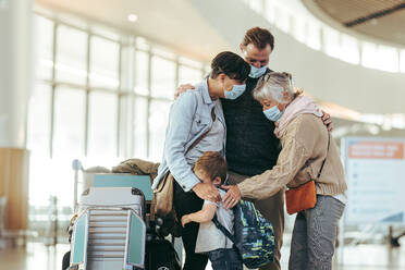 Eine ältere Frau begrüßt eine Familie, die nach der Pandemiesperre am Flughafen ankommt. Ein Ehepaar und ihr Kind werden von ihrer Mutter am Flughafen begrüßt. Alle tragen Gesichtsmasken. - JLPSF06613