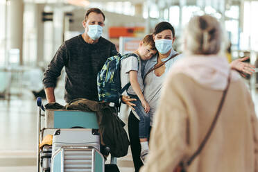 Ein Ehepaar und ihr Sohn treffen sich am Ankunftsgate mit ihrer Großmutter am Flughafen. Eine Familie kommt am Flughafen an, wo eine ältere Frau während einer Pandemie auf sie wartet. - JLPSF06615